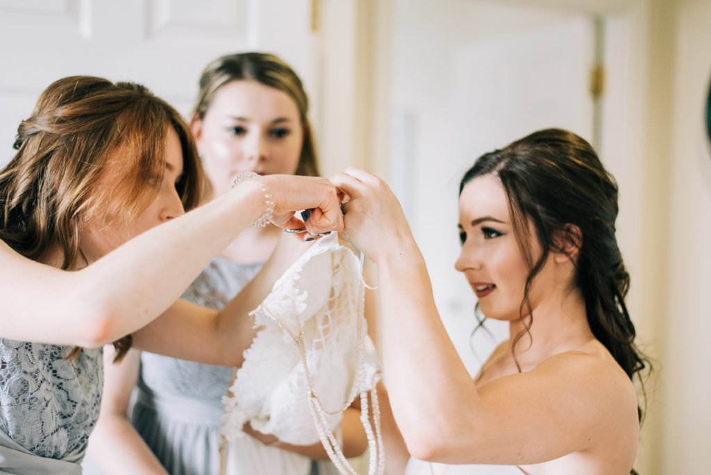 Bridesmaids help the bride into her wedding dress