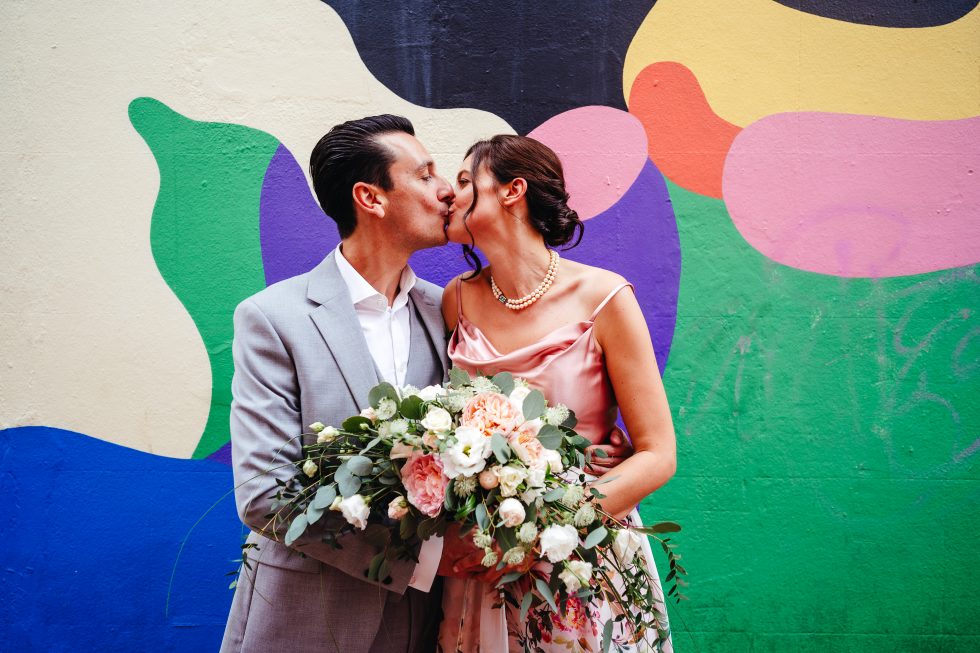 Couple kissing holding colourful wedding bouquet during colourful wedding in devob