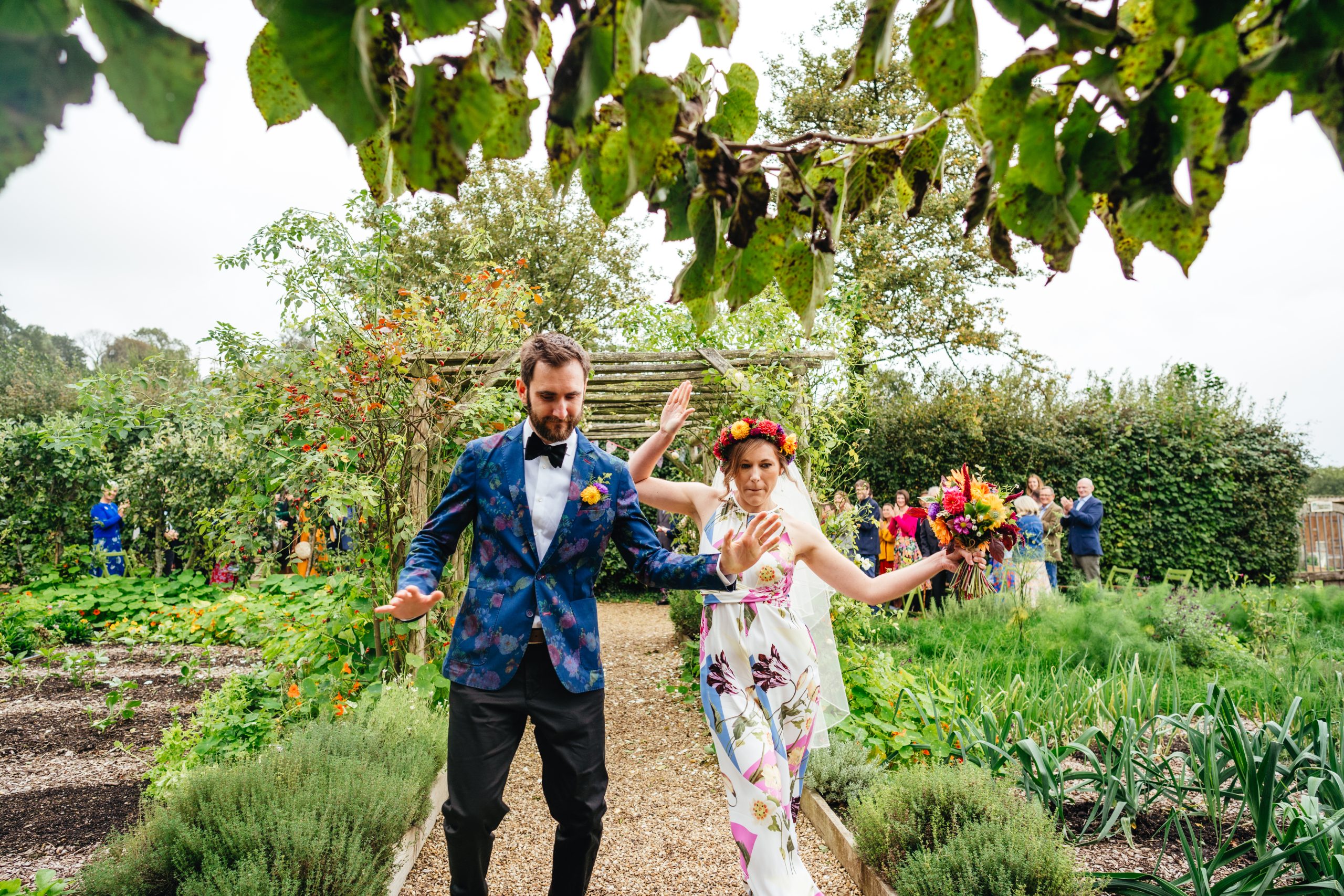 Bride and groom dressed colourfully dance down the aisle at Riverford Farm in Devon