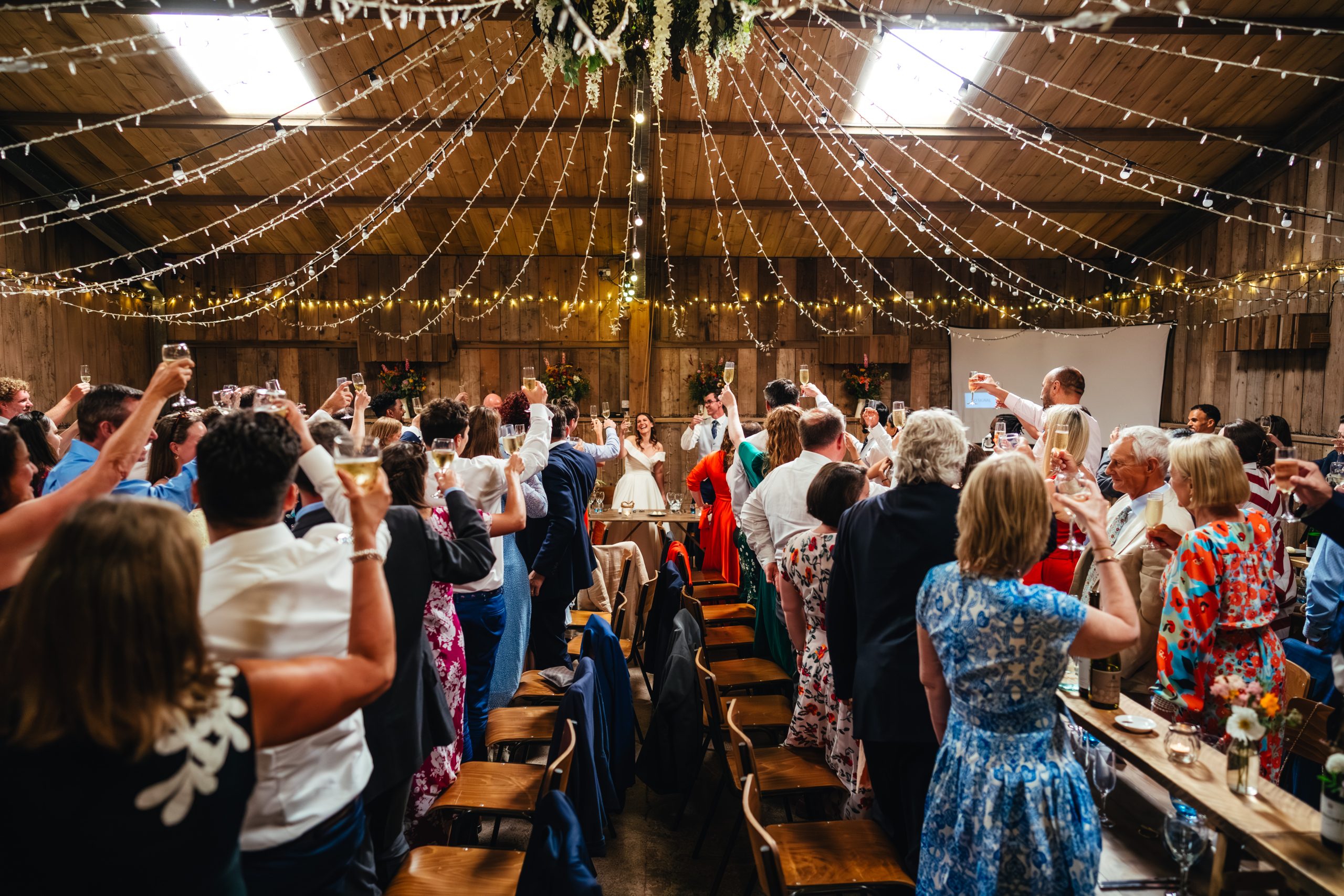 Guests cheers to the bride and groom inside the fairy light lit Devon wedding venue